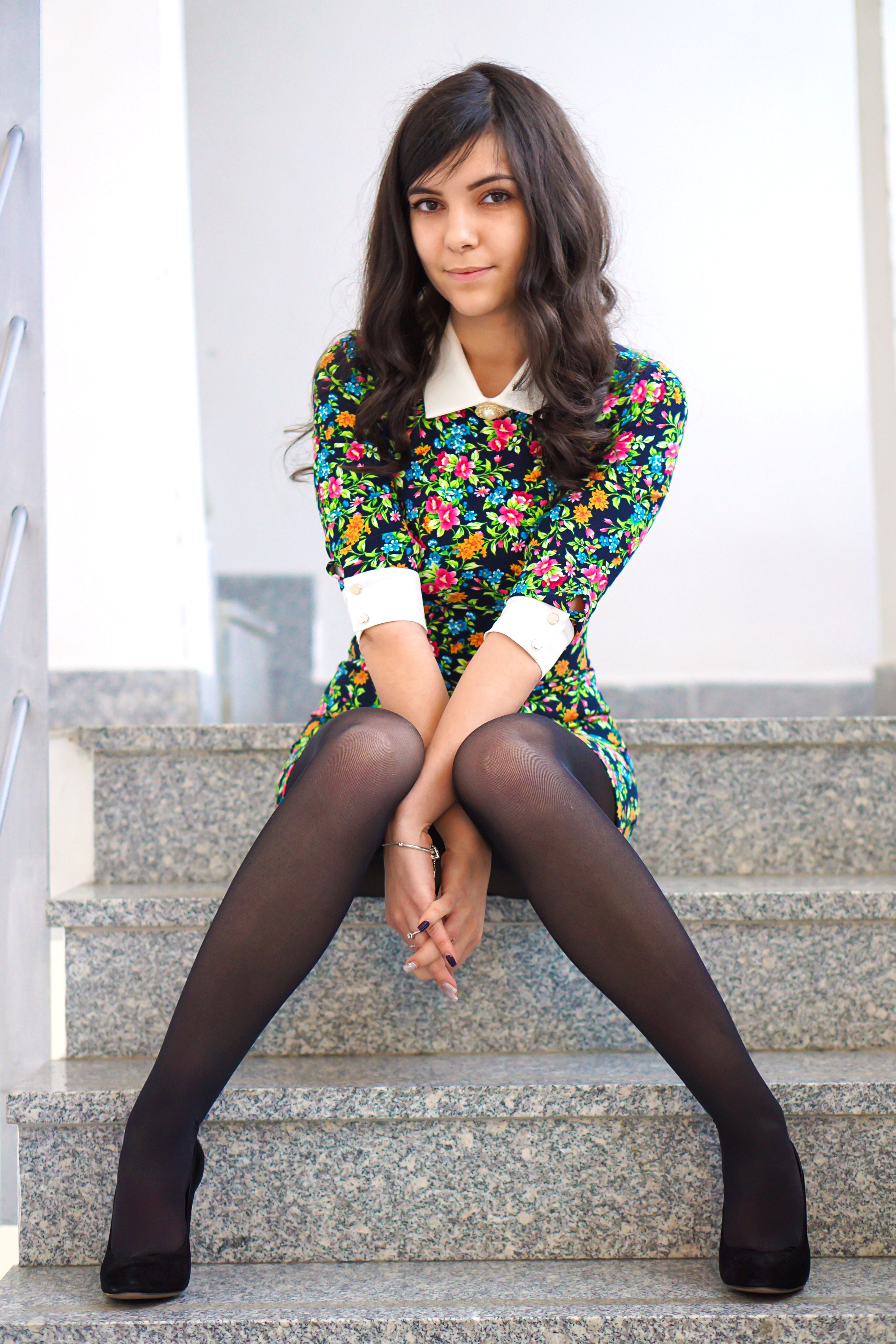 Free photo A dark-haired girl in a flowered dress sits on the steps