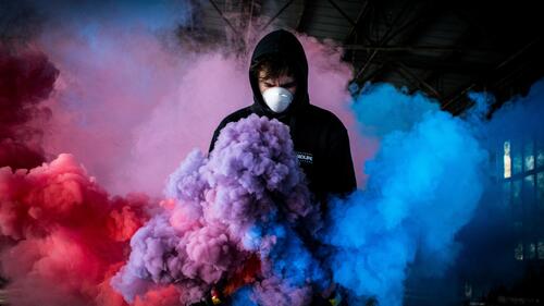 Masked guy standing in colored smoke.