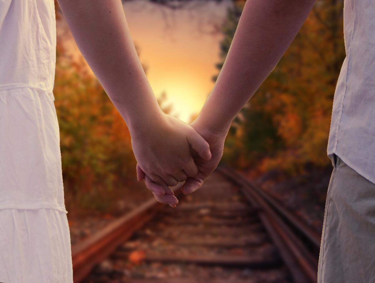 Young couple holding hands walking along the railroad tracks