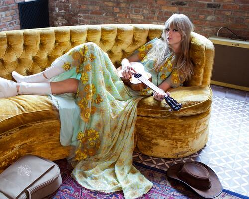 Taylor Swift lies on the couch with a guitar in his hands