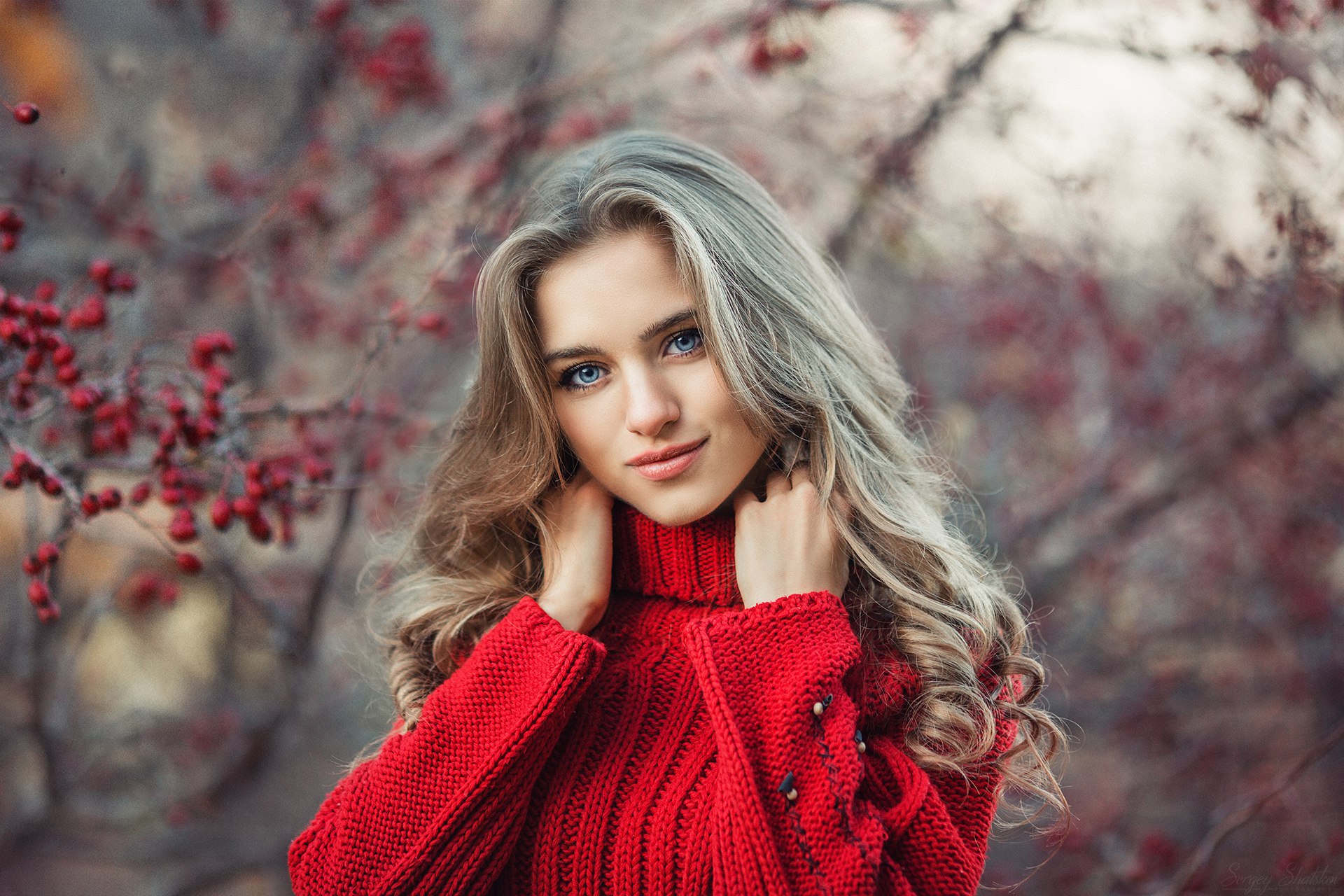 A girl in a red turtleneck poses against the background of a tree with rowanberries