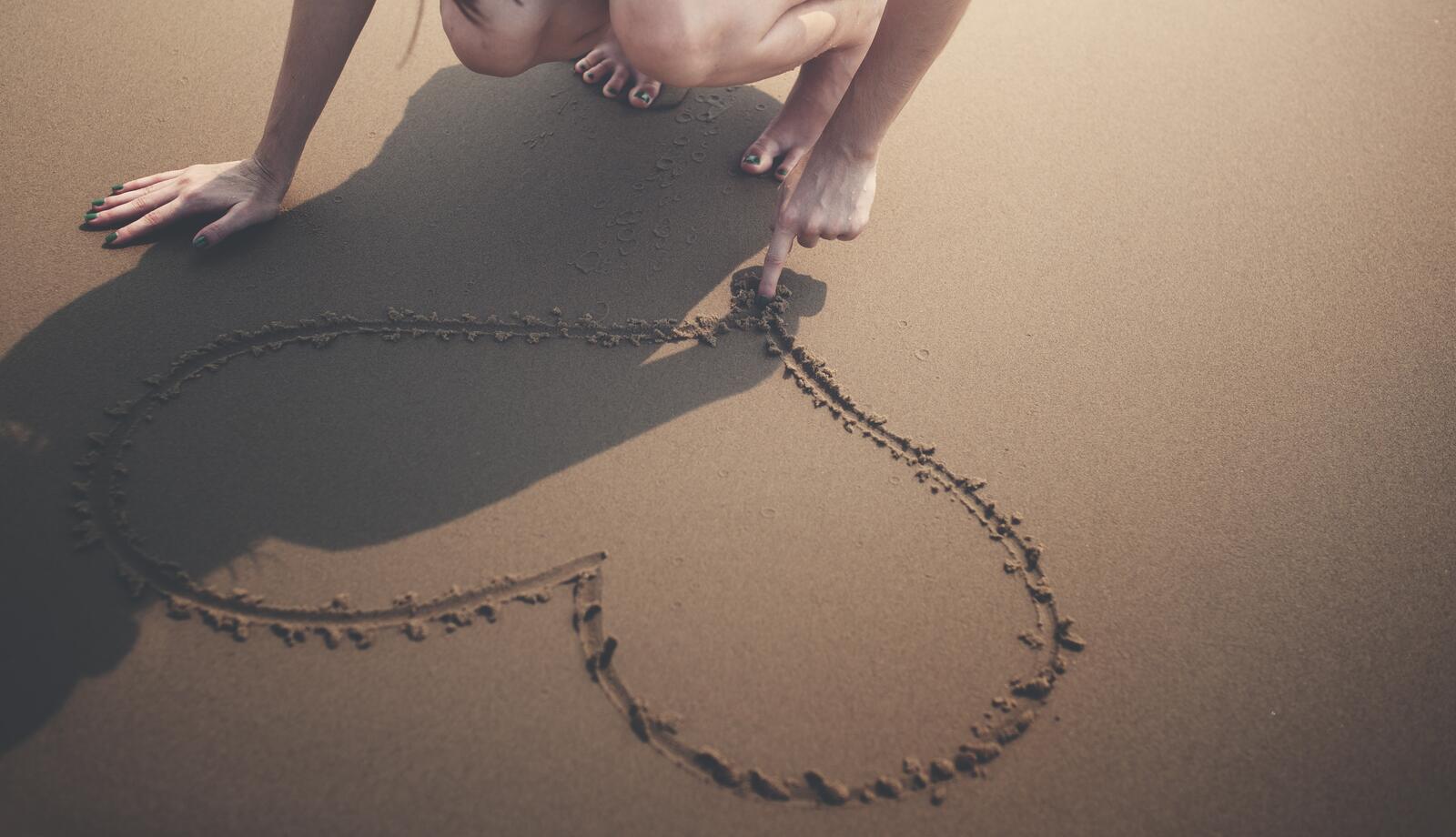 Free photo A girl draws a heart in the sand
