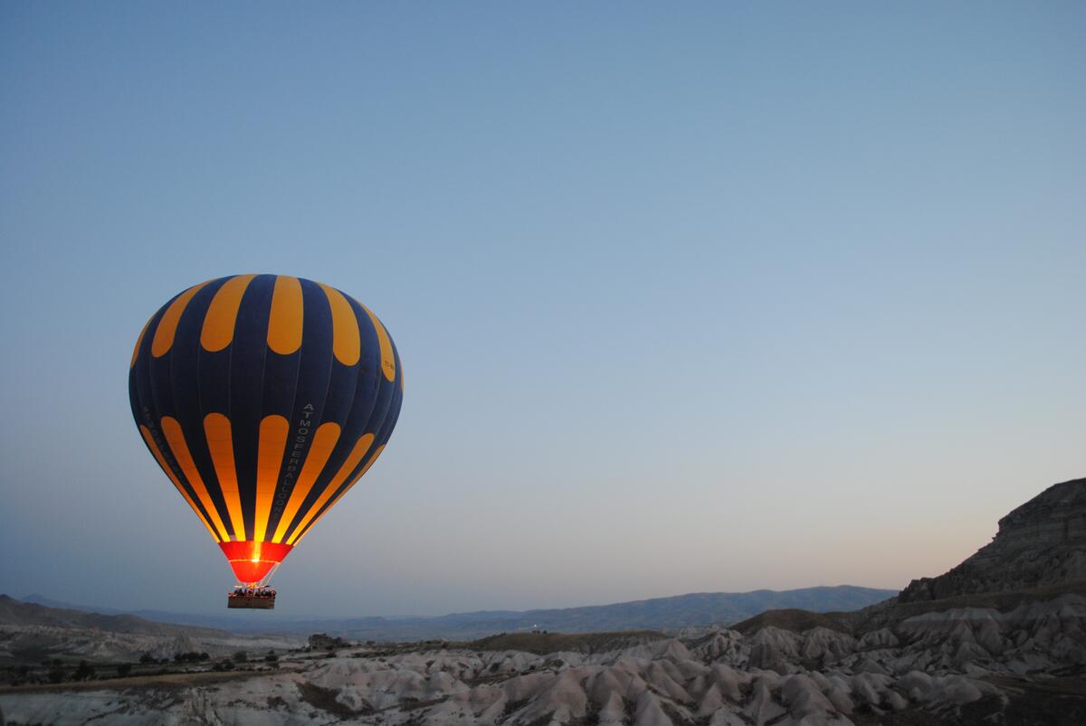 A hot air balloon flies over the ground in the evening.