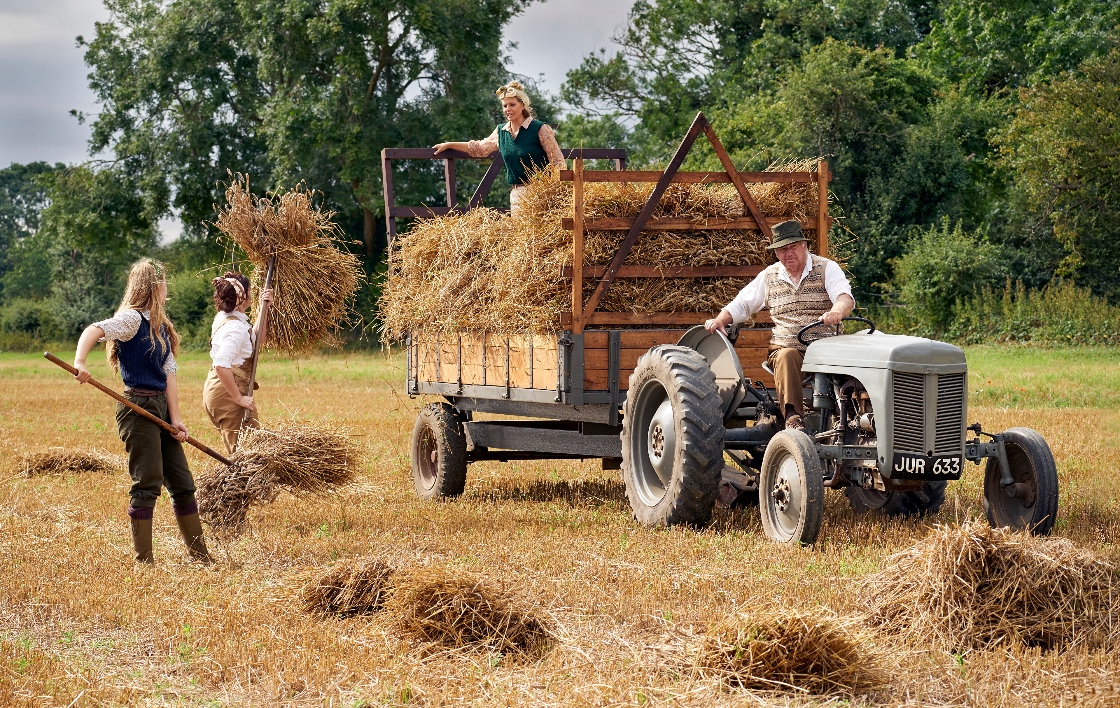 Фермер с девушками на тракторе собирает высохшее сено