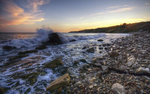 Waves crash against the rocky shore during sunset