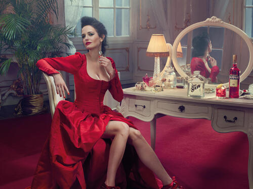 Eva Green sits in a red dress at a table with a mirror