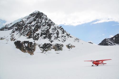 Красный частный самолет приземлился в горах Арктики на снегу