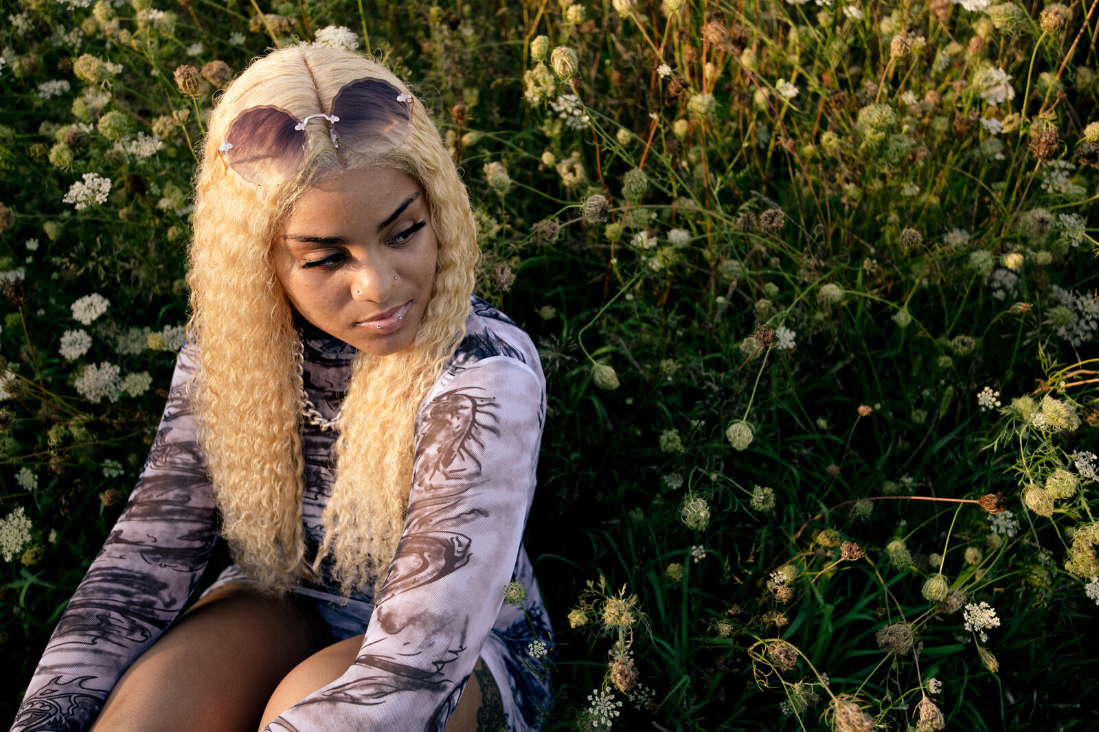 Free photo A dark-skinned girl with white hair sits by a bush with flowers