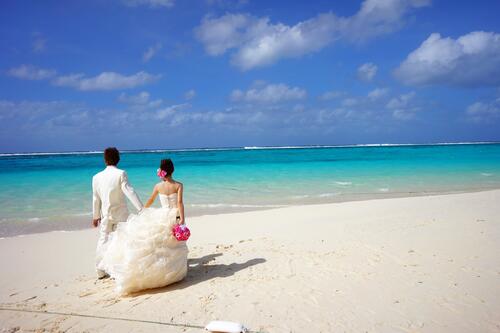 A wedding couple walks on a white beach