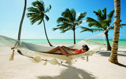 Sunbathing on a hammock tied to palm trees on the beach.
