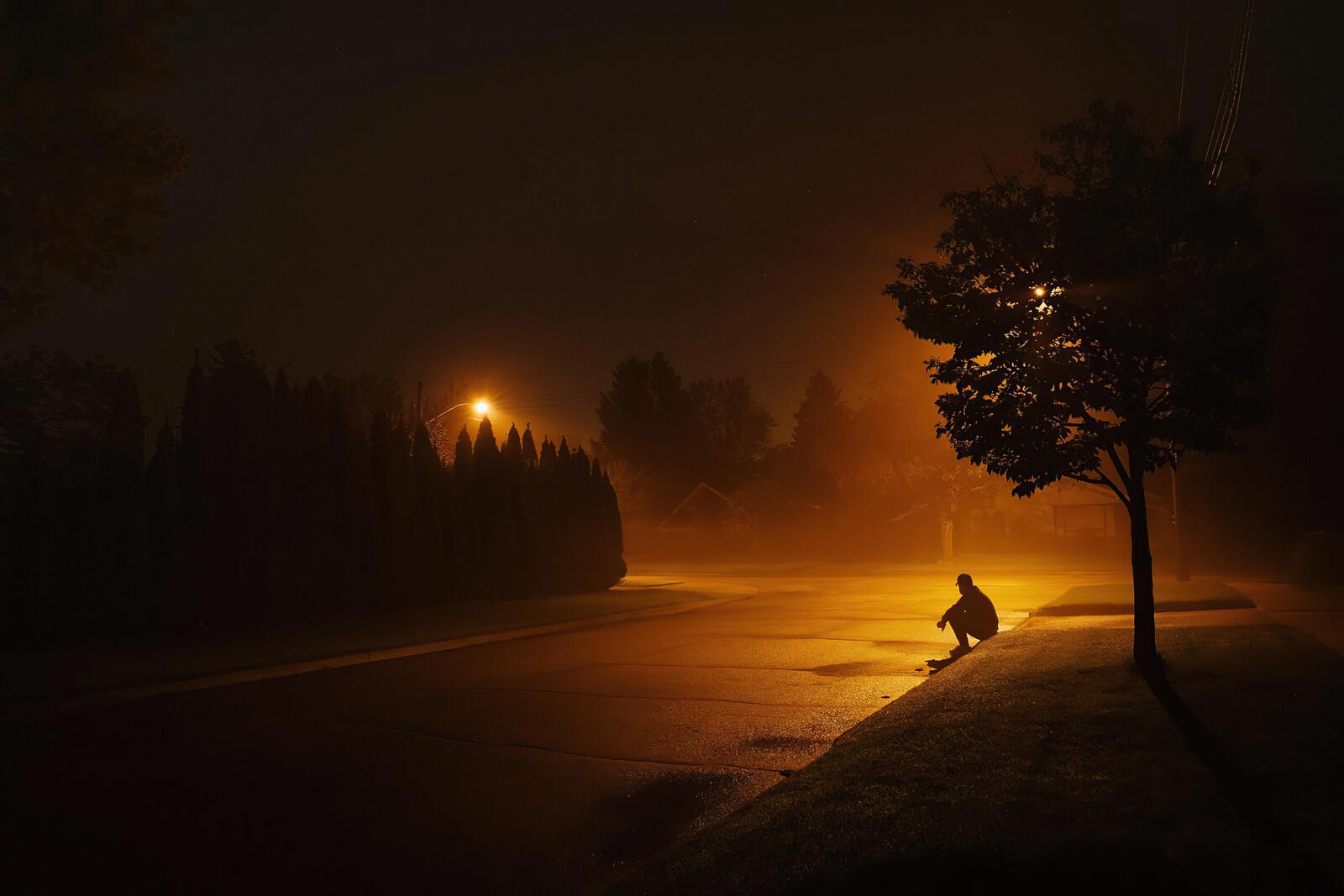 Бесплатное фото Одинокий мужчина сидит на поребрике дождливой ночью