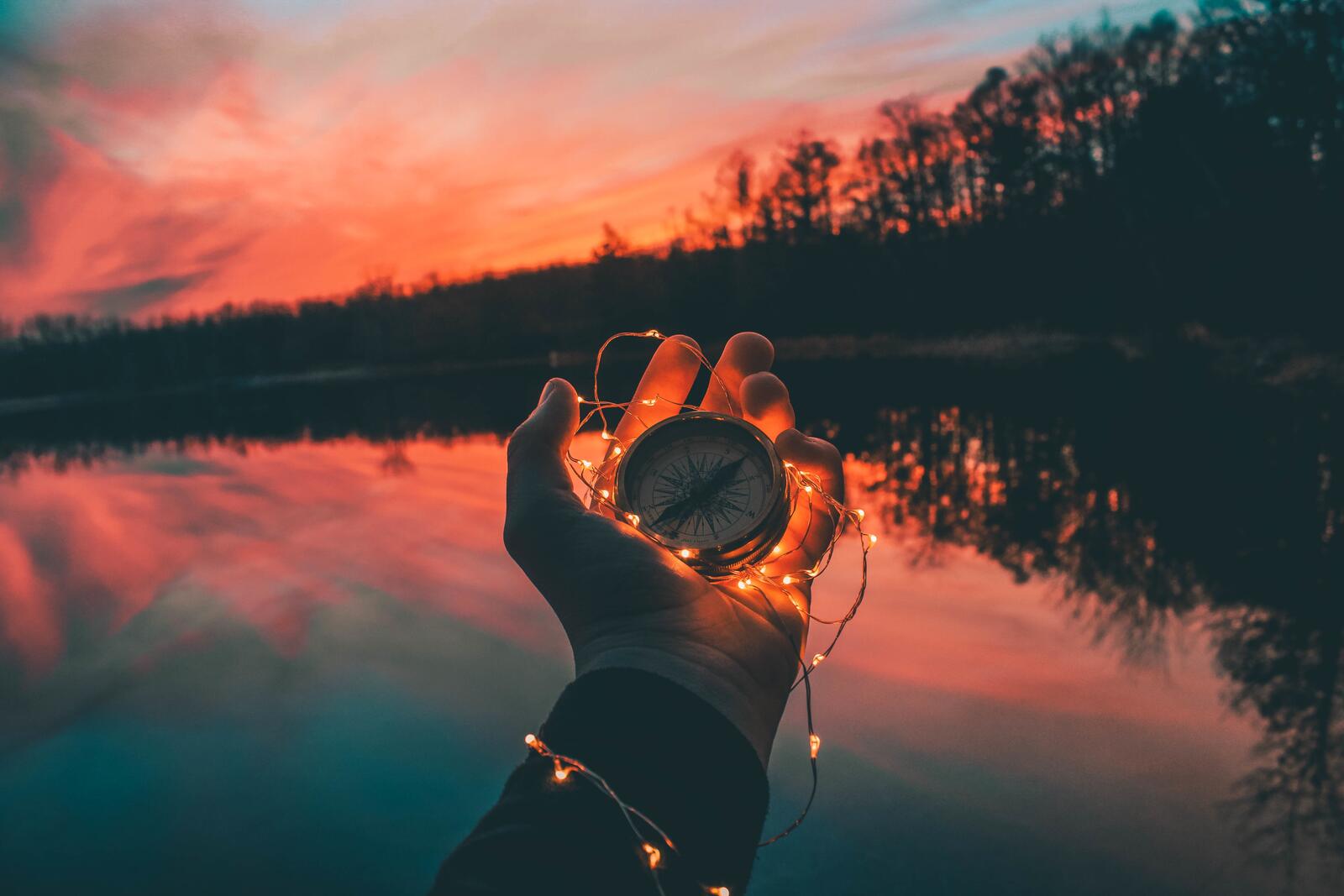 Бесплатное фото Компас в руке на фоне озера с гирляндой