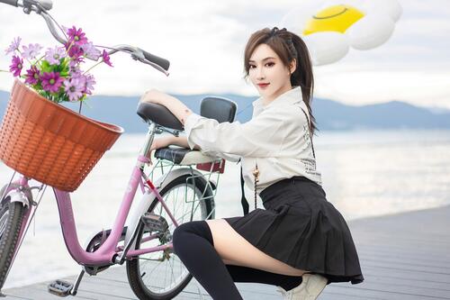 Китайская фотомодель Чжоу Янь Си в черной миниюбке и гольфах на берегу присела рядом с велосипедом