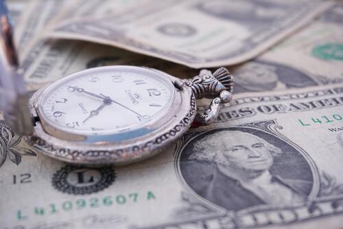 A pocket watch made of silver lies on dollar bills