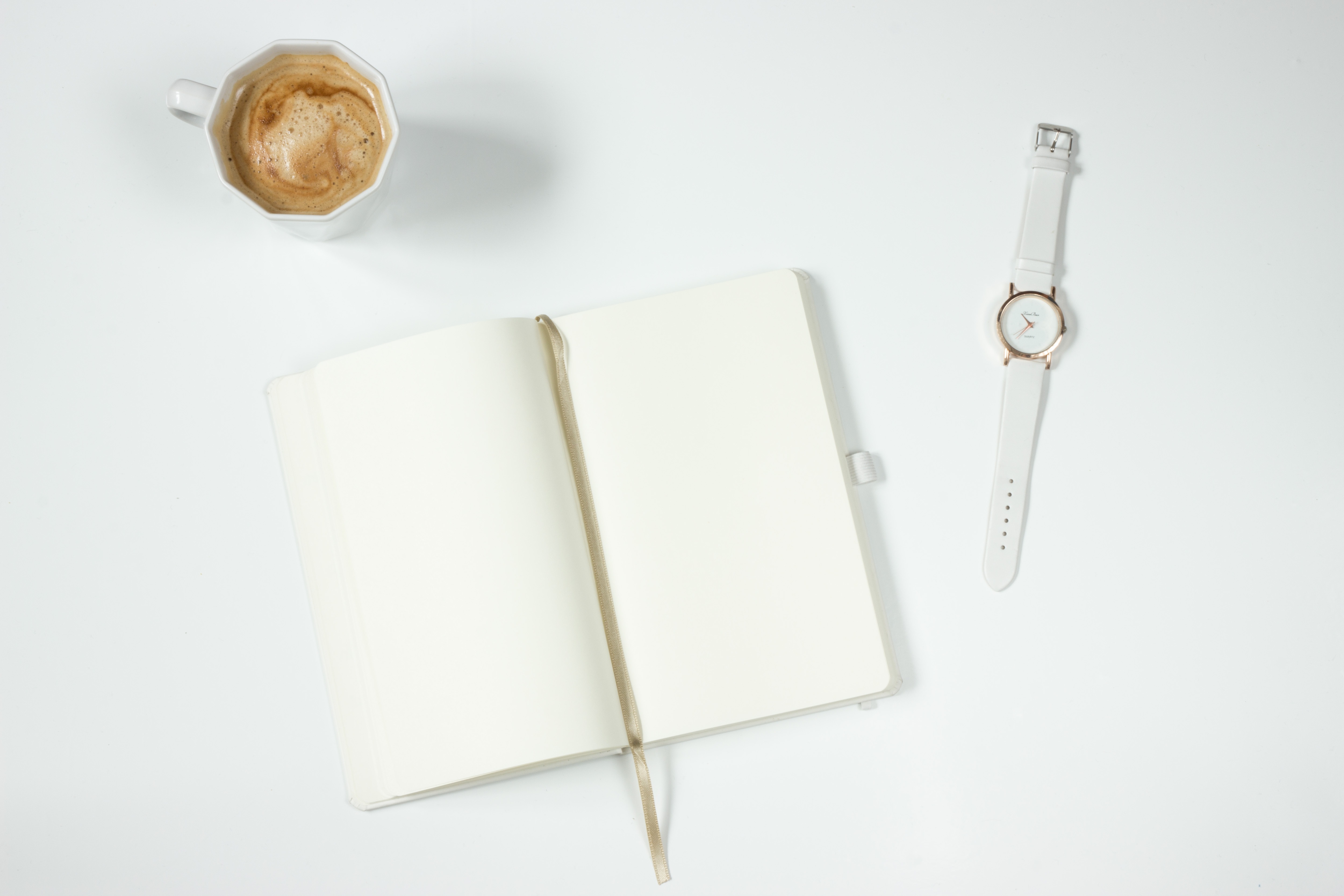 一张白色的桌子上有一本笔记本、一个咖啡杯和一个时钟