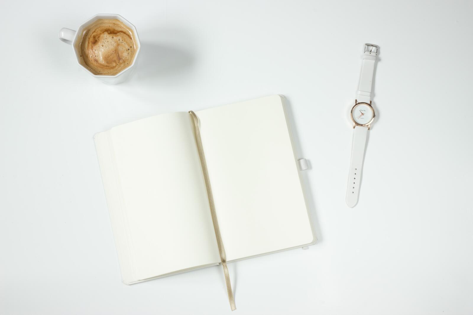 Free photo A white table with a notebook, a coffee mug, and a clock