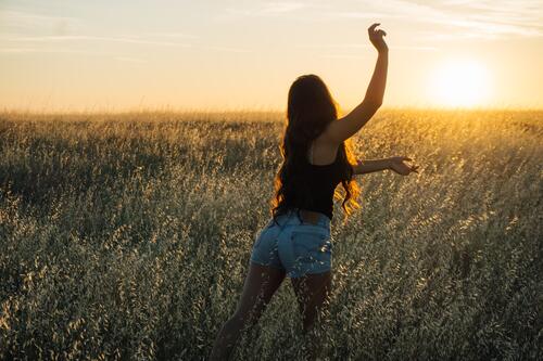 Девушка позирует в поле на фоне яркого солнца уходящего в закат