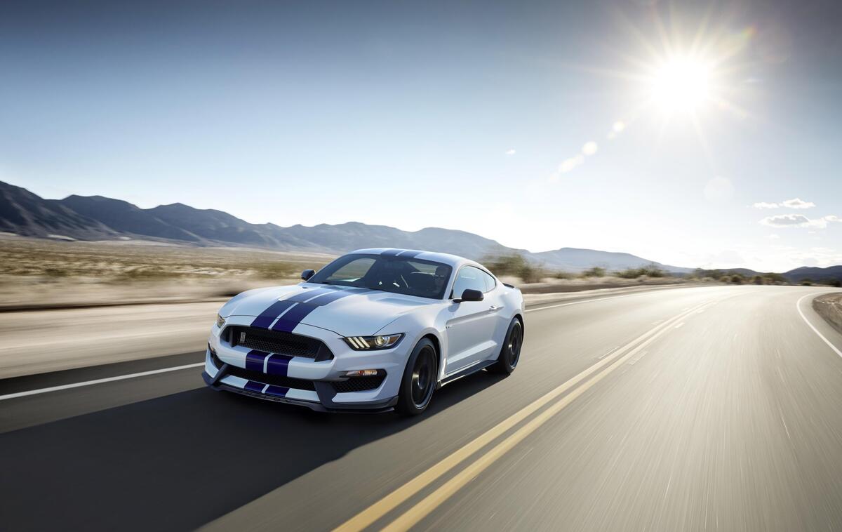A white Ford Mustang with blue stripes driving down a country road.