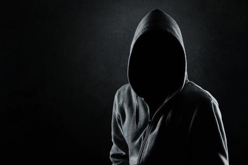A guy in the darkness with a hidden face in a hooded sweatshirt.