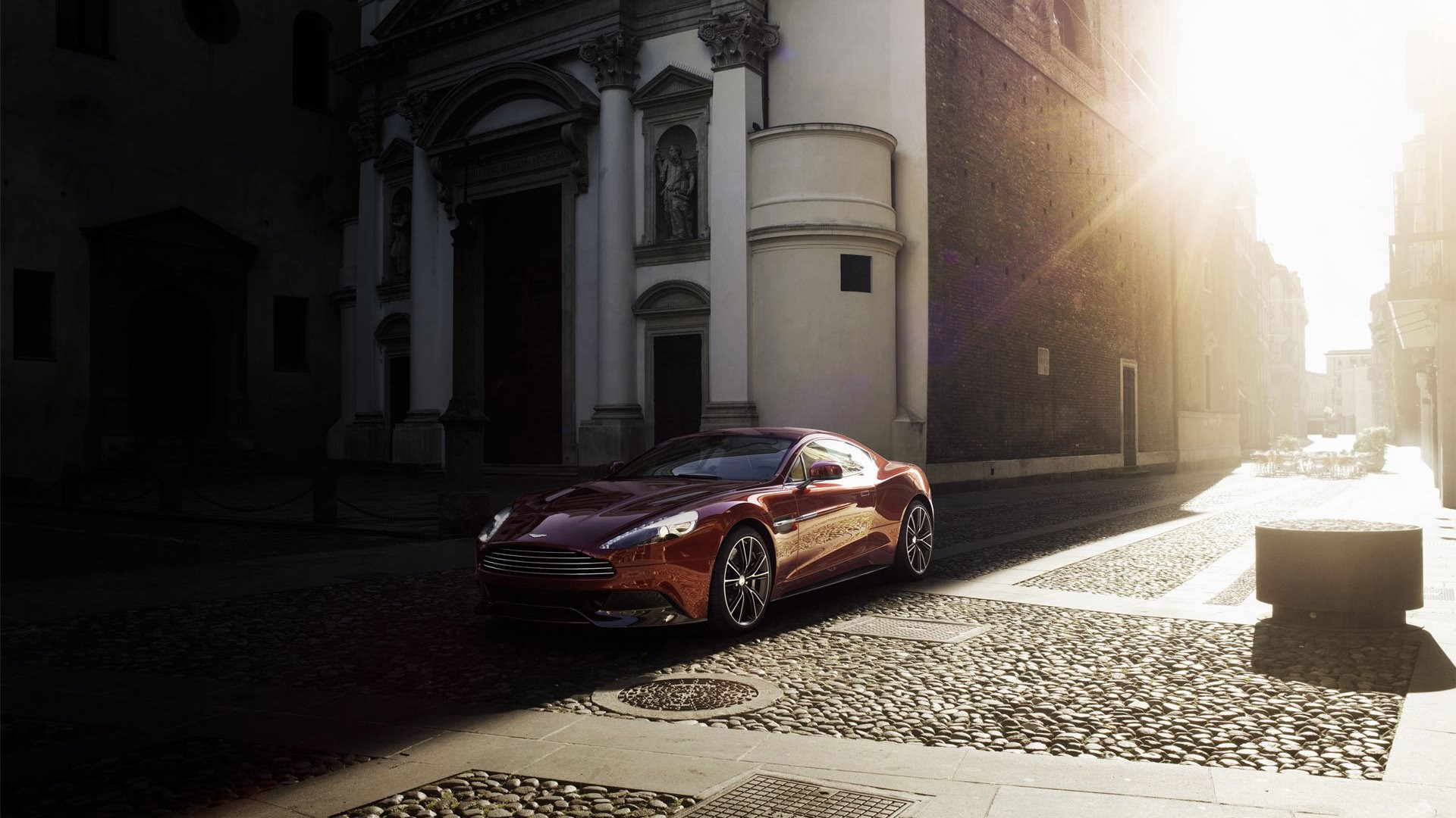 The Aston Martin Vanquish drives down a sunny street.