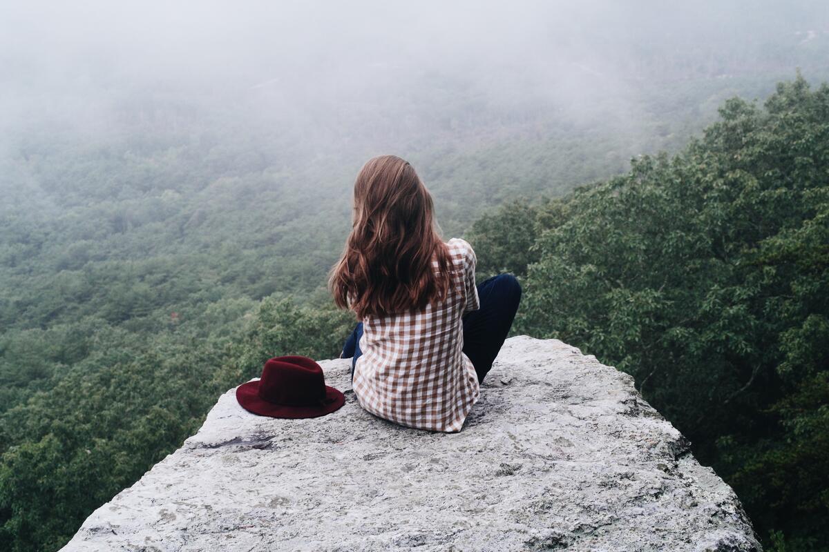 A girl sitting on a cliff face looking off into the distance.