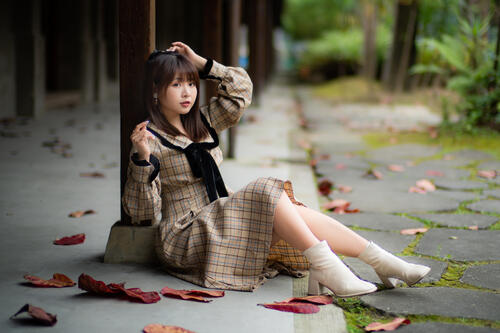 Азиатка сидит на бетоне рядом с опавшими листьями