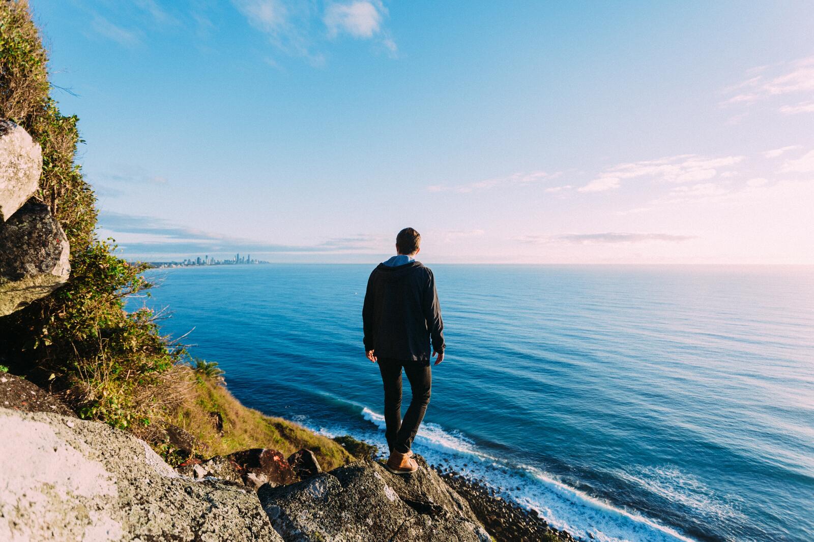 Бесплатное фото Парень стоит на берегу любуясь морским пейзажем