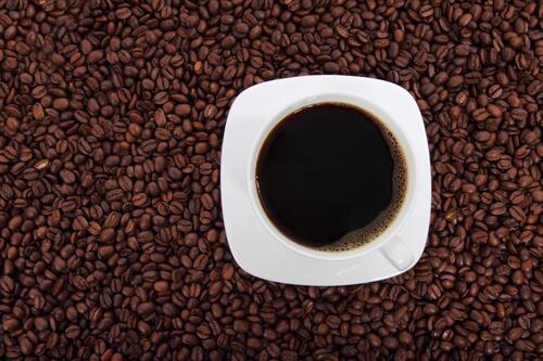 White mug with coffee and saucer on the background of a coffee bean