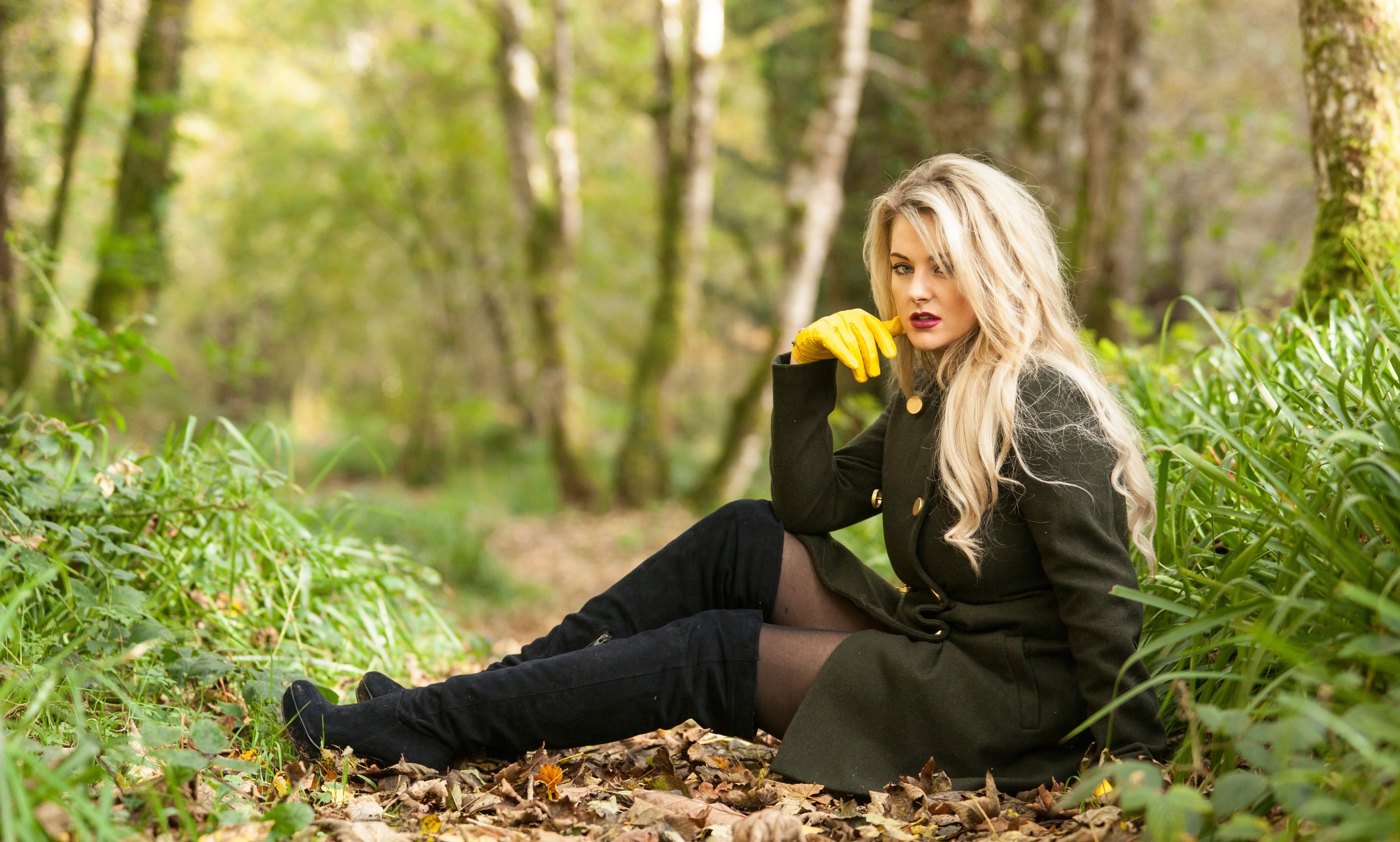 Free photo A blonde-haired girl in a green coat sits on fallen leaves