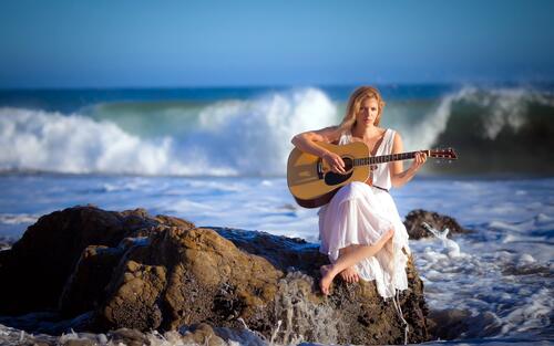 Девушка в белом платье с гитарой у берега моря