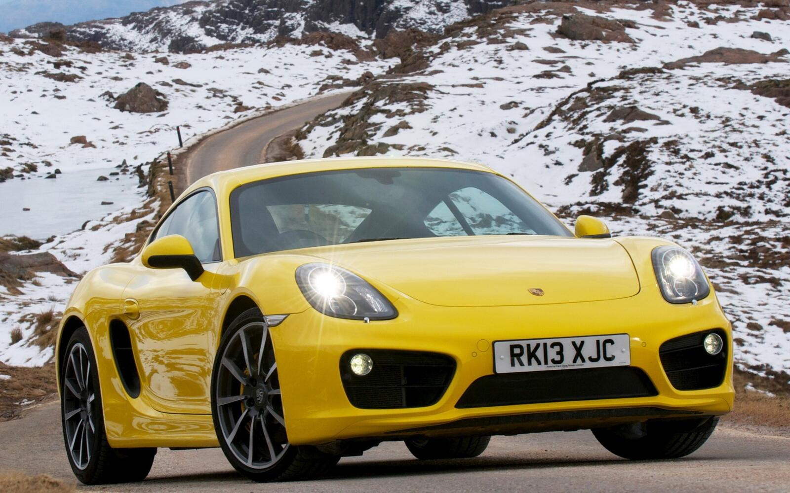 Free photo A yellow Porsche Boxster against a backdrop of snowy mountains.