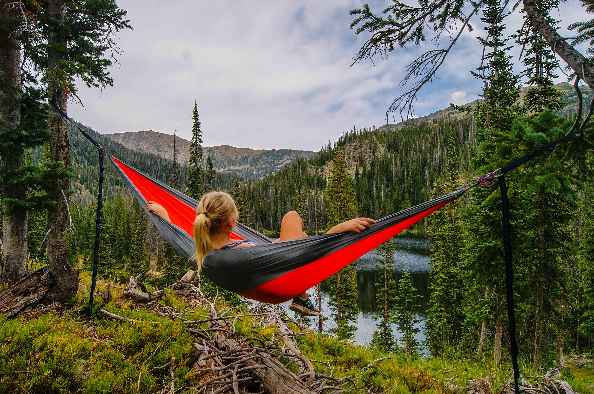 A girl lying on a hammock overlooking a forest lake