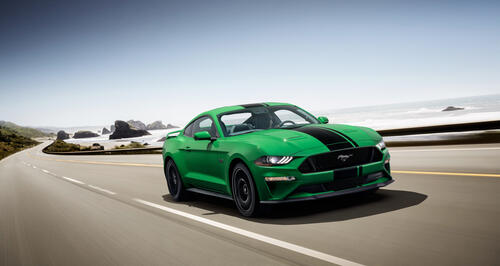 A green-colored 2018 Ford Mustang drives down a country highway