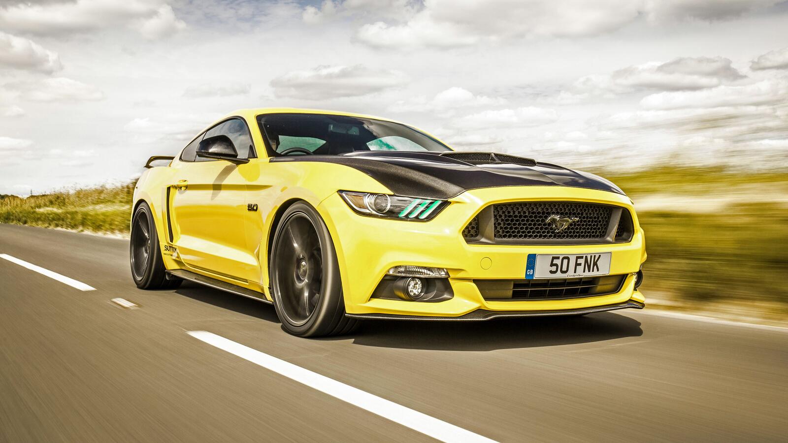 Free photo A yellow Ford Mustang with a black hood rushes down the road