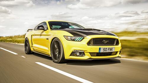 A yellow Ford Mustang with a black hood rushes down the road