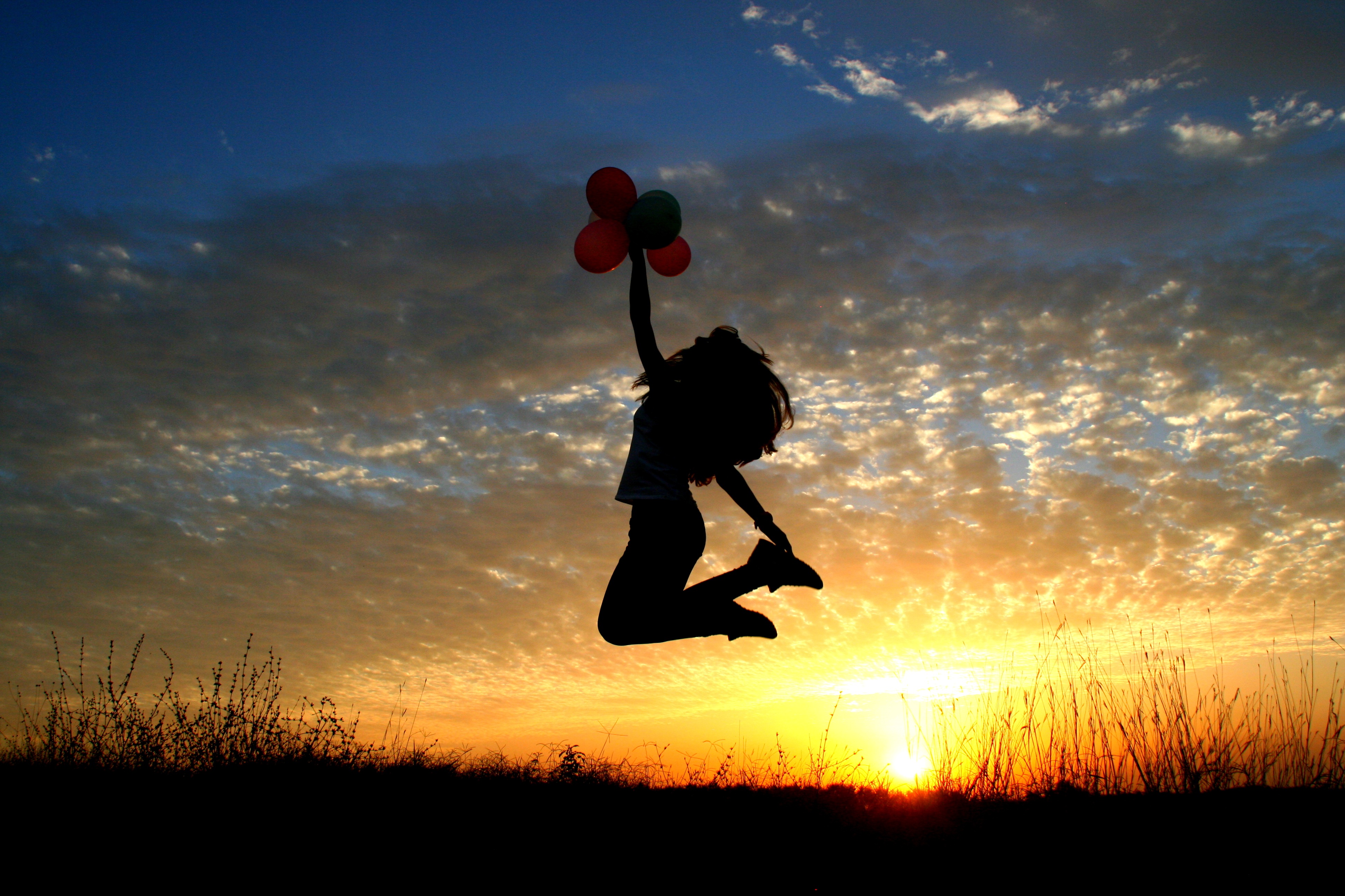 Силуэт девушки прыгающей вверх с воздушными шариками на закате дня