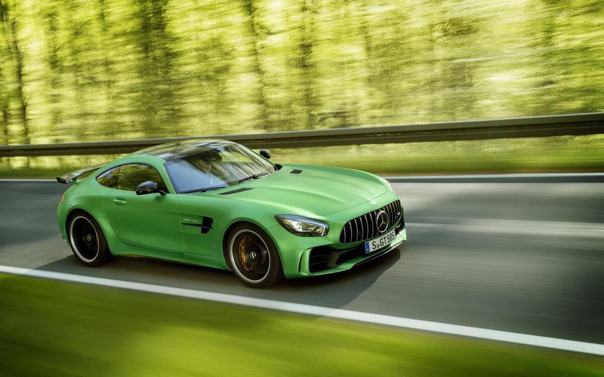 A green Mercedes amg gt r driving down a forest road.