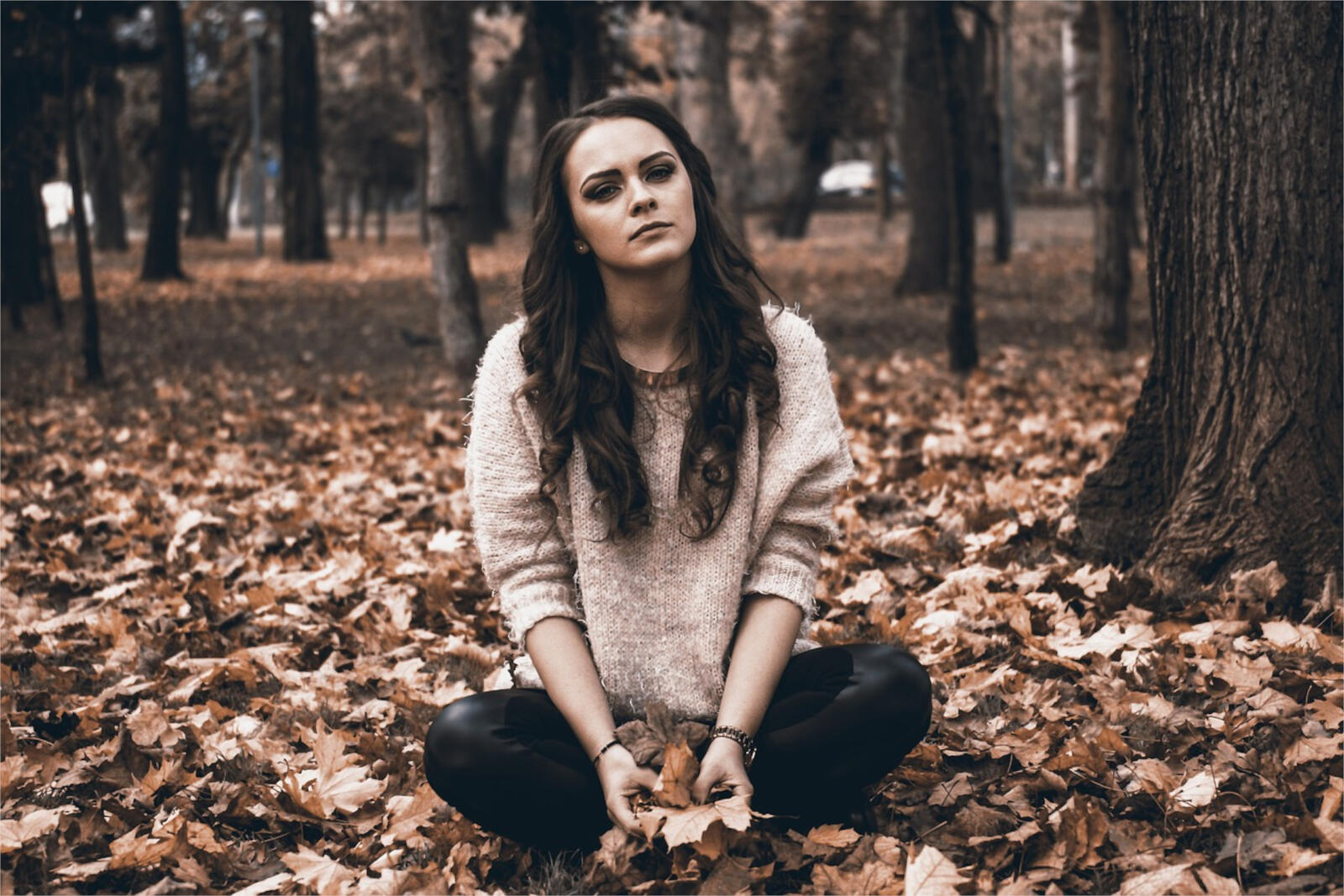 Free photo Young brunette sitting on fallen autumn leaves