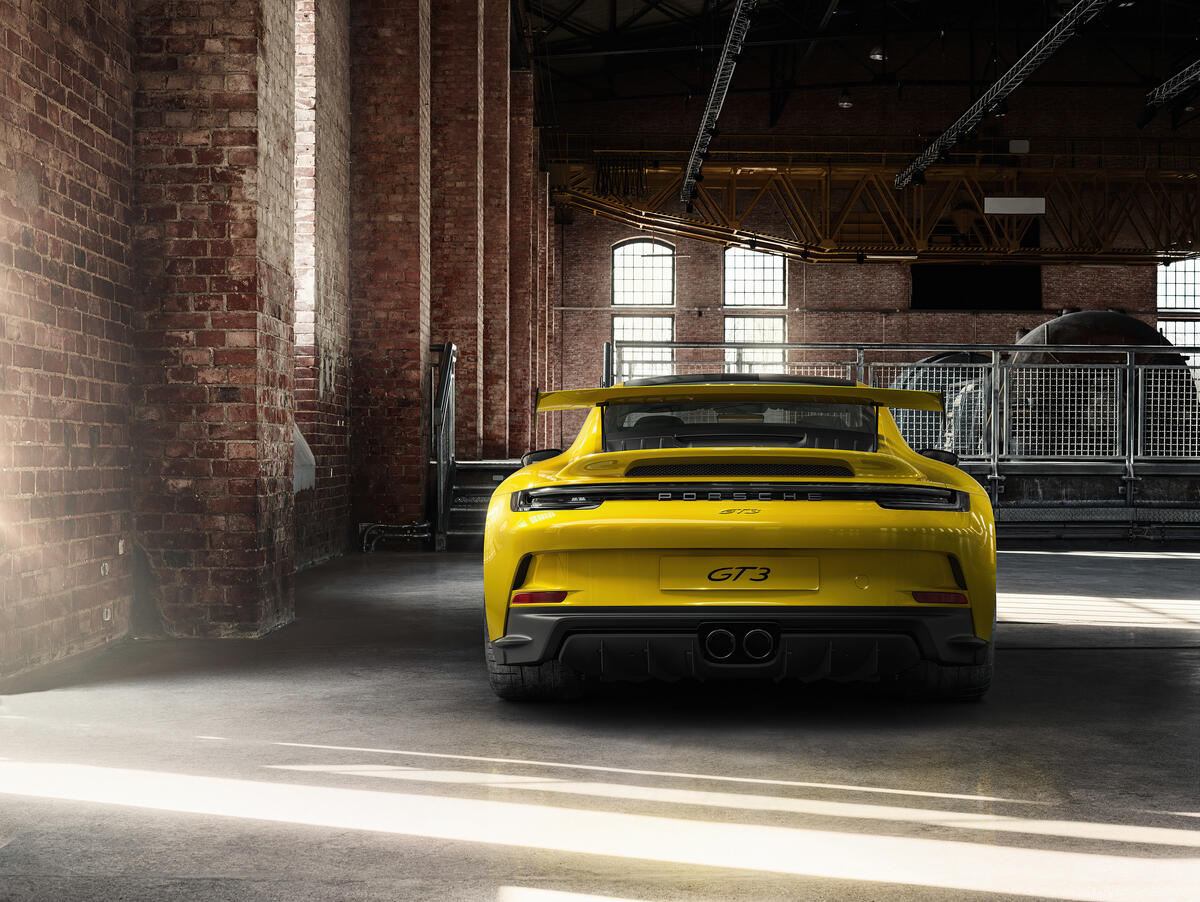 Желтый Porsche 911 сфотографированный сзади в ангаре из красного кирпича