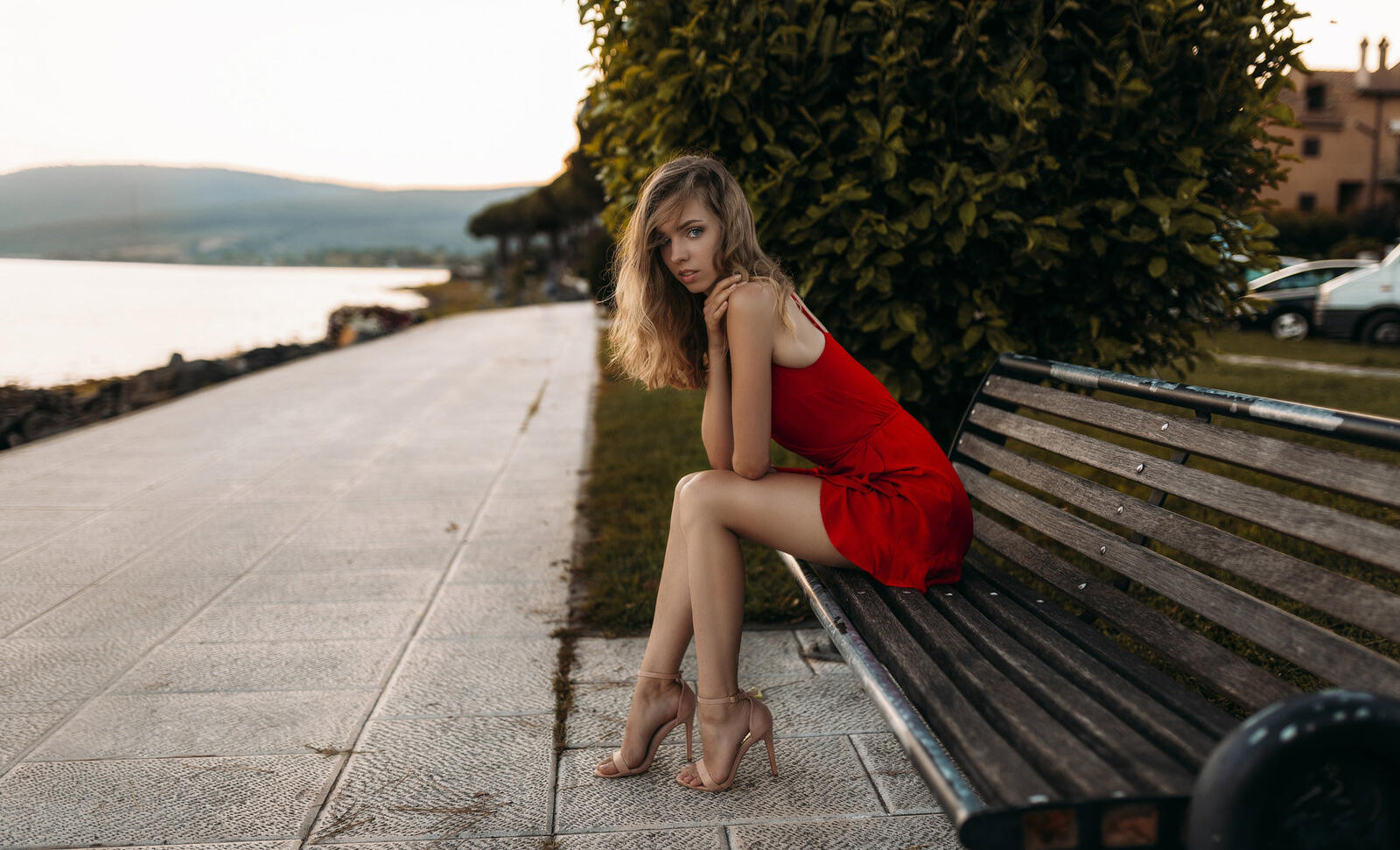 Free photo A beautiful model in a red dress sits on a bench