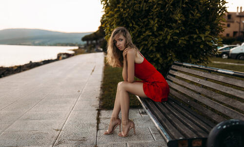 Красивая модель в красном платье сидит на лавочке