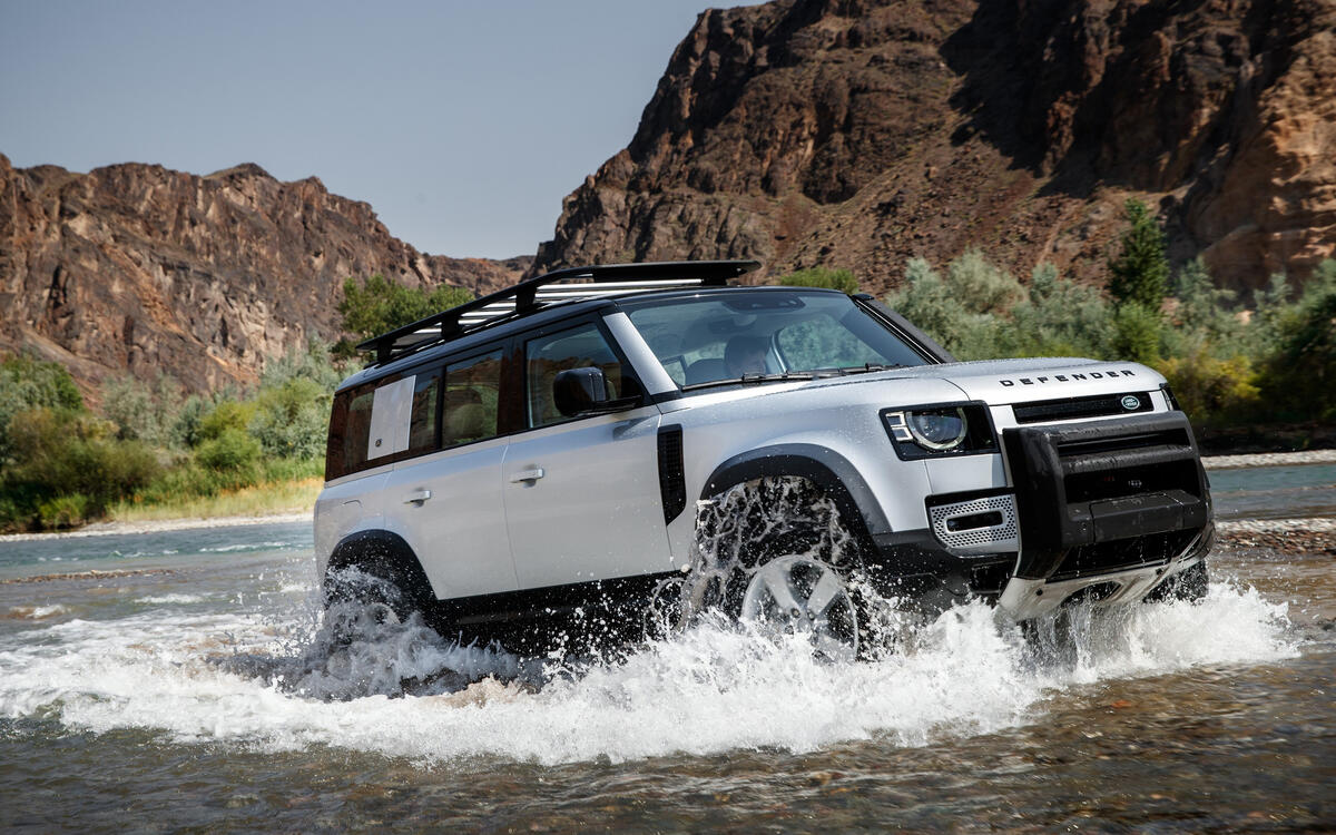 A white Land Rover Defender wading through a river