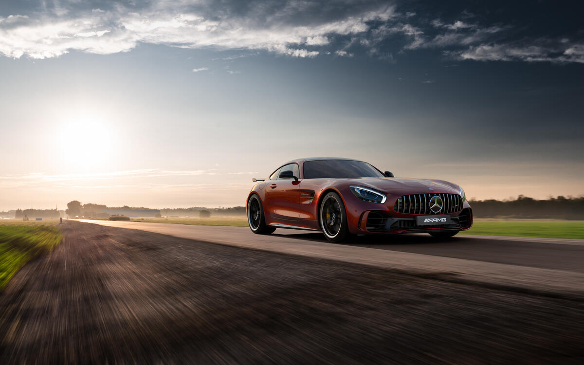 Red Mercedes AMG GTR driving down the road at sunset
