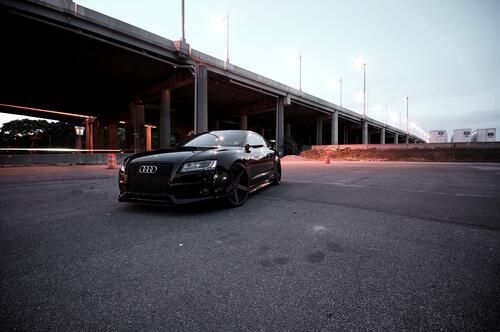 A black Audi rs5 is parked under a bridge.