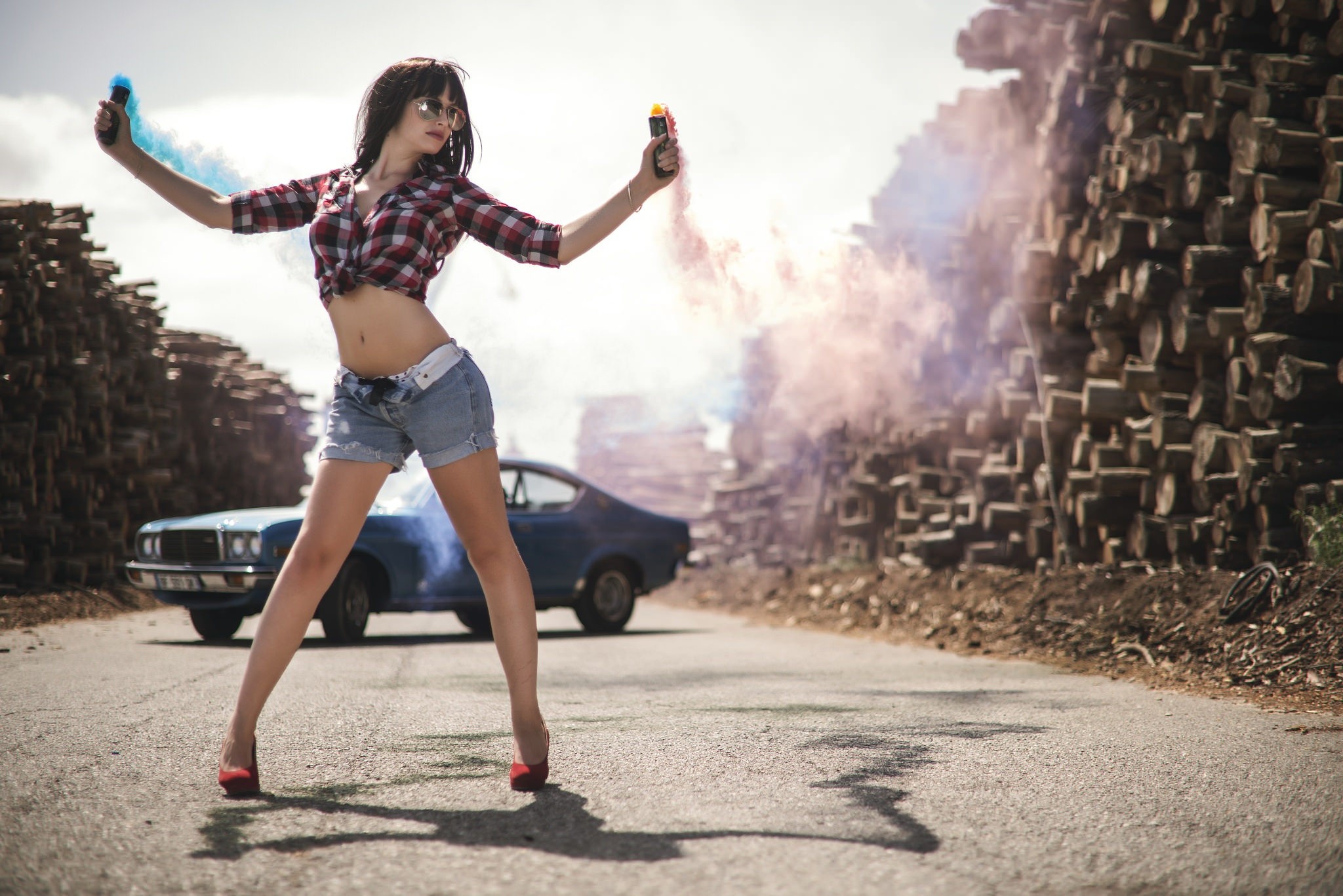Девушка в коротких шортах стоит на фоне машины с дымовыми шашками вруках