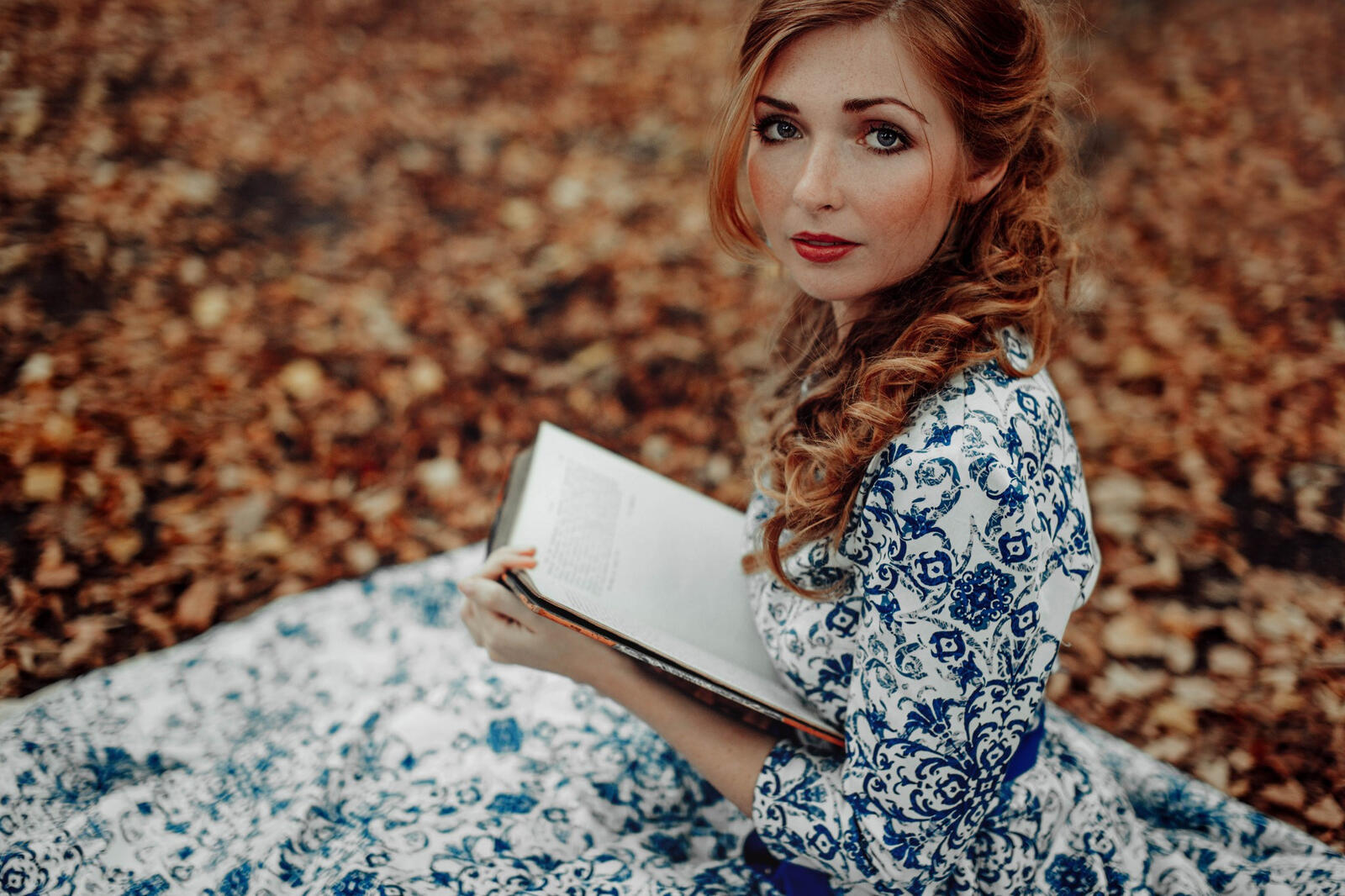 Free photo A girl in a white dress with blue patterns reads a book