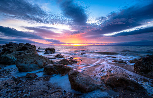 Скалистый берег моря и красочный закат на голубом небе