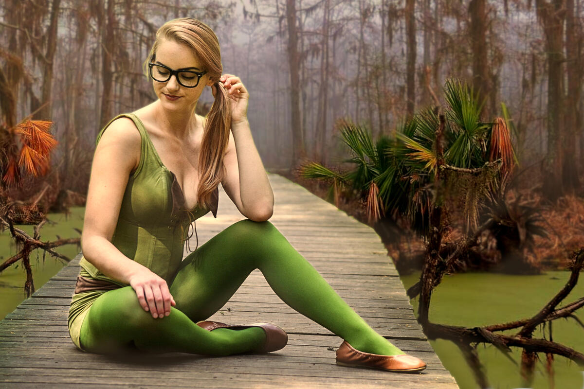 Блондинка в зеленом сидит на мостике через болото