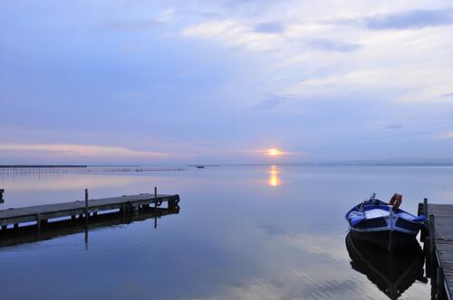 Восход солнца на озере у пристани с деревянной лодкой