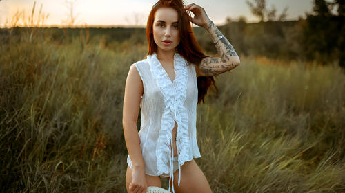 With a tattoo on her arm undressing in the field.